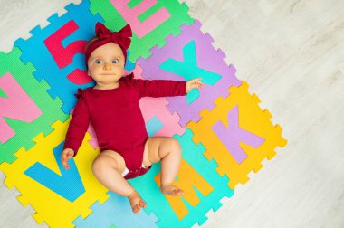 View from above of a little baby girl lay on the color abc carpet with letters and numbers