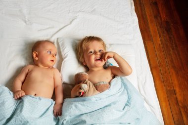 Little kids, boy and girl, babies lay in a bed waking up view from above