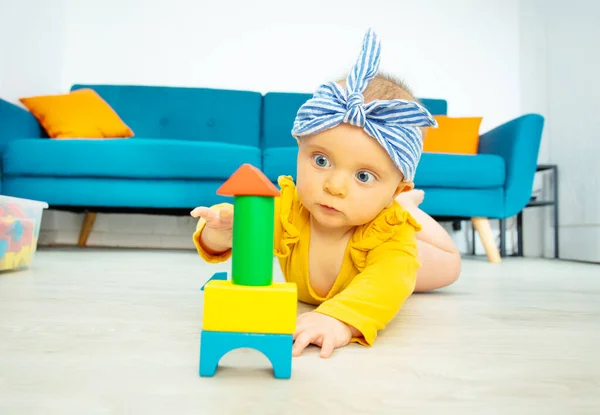 かわいいです赤ちゃん女の子遊びます色の木製ブロック作りますタワーリビングで笑顔 黄色の体と弓を身に着けています — ストック写真