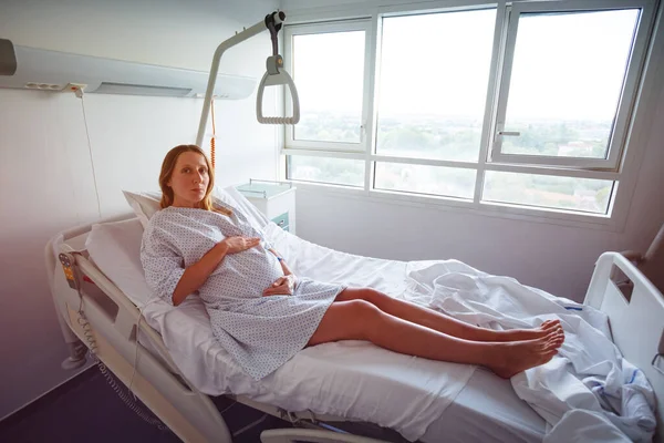 笑顔妊娠中の女性で病院のベッドホールド大きな腹とともに手 — ストック写真