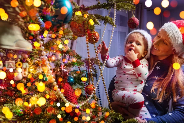 在圣诞树旁 母亲带着蹒跚学步的儿子快乐地望着戴着圣诞帽的装饰 — 图库照片