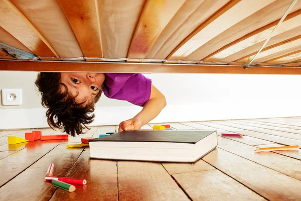 Хлопчик Знаходить Книгу Під Ліжком Спираючись Вниз Дивлячись Камеру — стокове фото