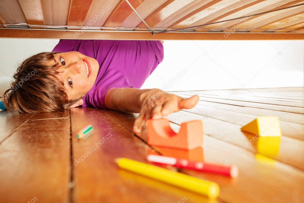 Boy stretch to reach color toy block under the bed, funny upside down photo