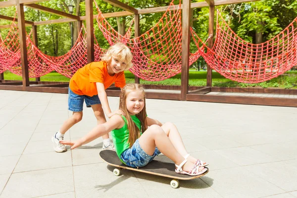 Boy pushes girl on skateboard — Stock Photo, Image