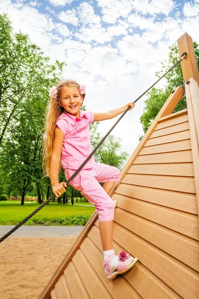 Happy girl climbs on wooden construction — Stock Photo, Image