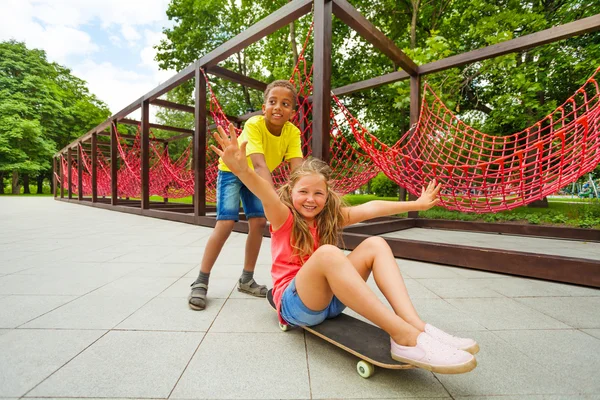 Boy pushes girl on skateboard — Stock Photo, Image