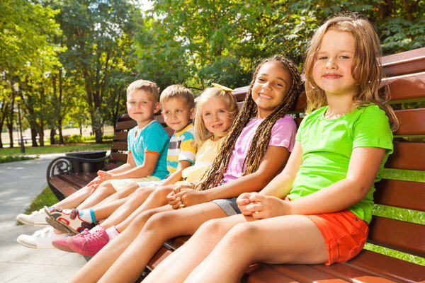 Мальчики и девочки сидят на скамейке
