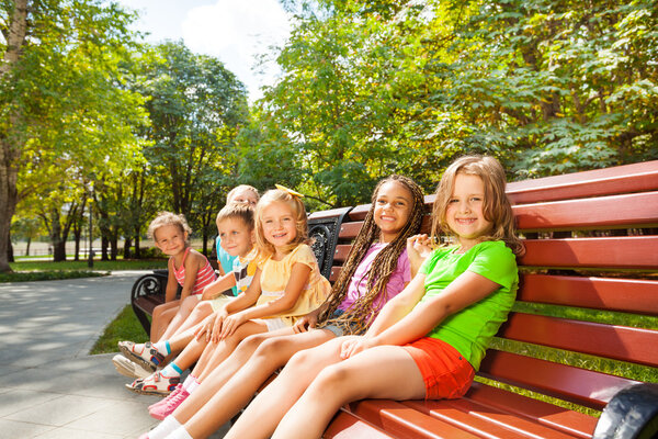 Мальчики и девочки сидят на скамейке
