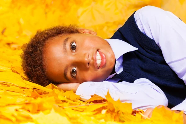 Smiling boy laying in leaves — Stock Photo, Image