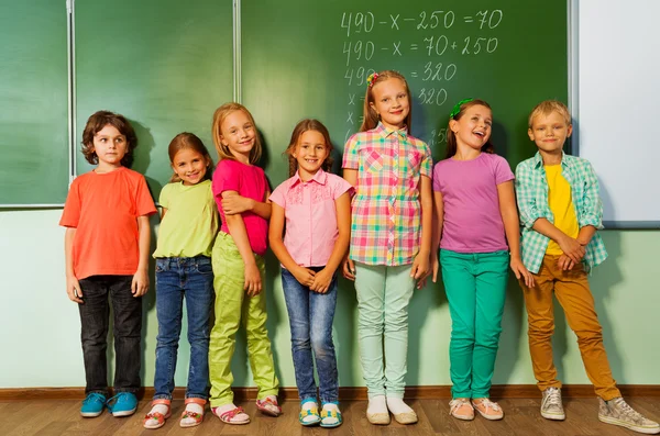 Kids stand in line near the blackboard — Stock Photo, Image