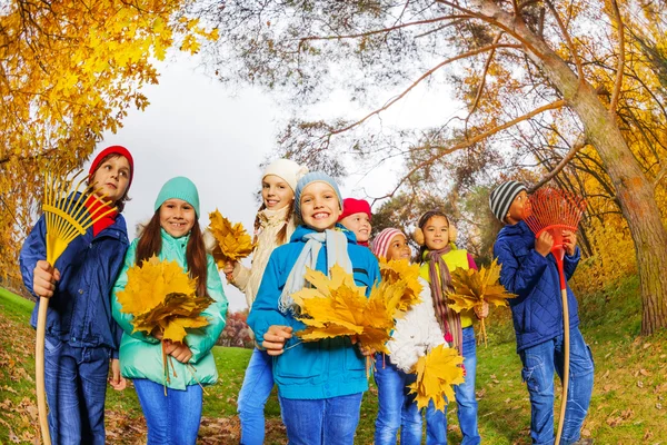 Crianças felizes com ancinhos e folhas — Fotografia de Stock