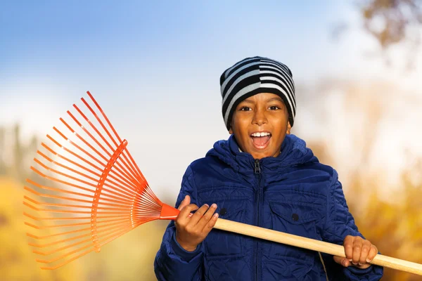 Boy holds red rake in park — Stock Photo, Image