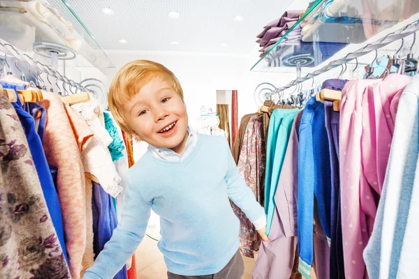 Blondes kleines Kind steht zwischen Kleiderbügeln — Stockfoto