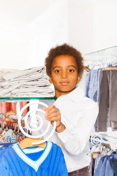 Afrikaanse jongen tussen rijen met kleren — Stockfoto