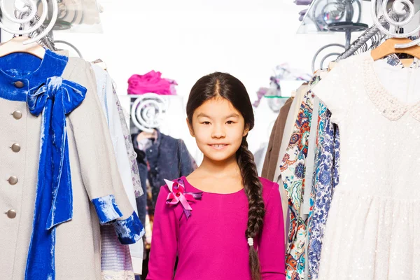 Meisje met vlecht staat tussen kleding — Stockfoto