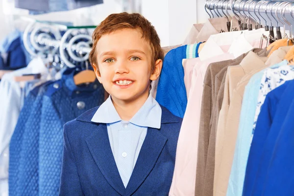 Boy standing near clothes on hangers — Stock Photo, Image