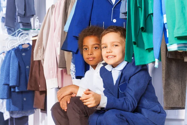 Meninos sentados perto de roupas em cabides — Fotografia de Stock