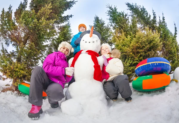 Crianças sentadas perto de boneco de neve — Fotografia de Stock
