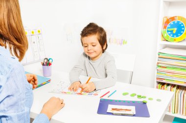 Boy colors shapes during ABA with therapist near