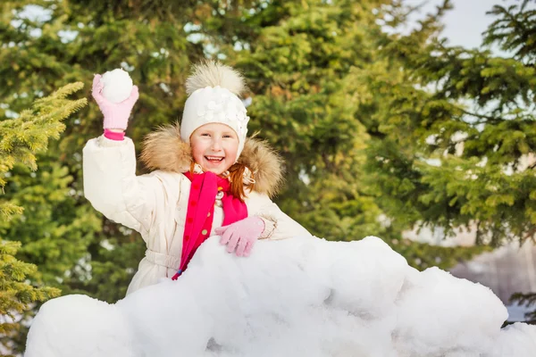 Dívka s sněhová koule za sněhu zdí — Stock fotografie