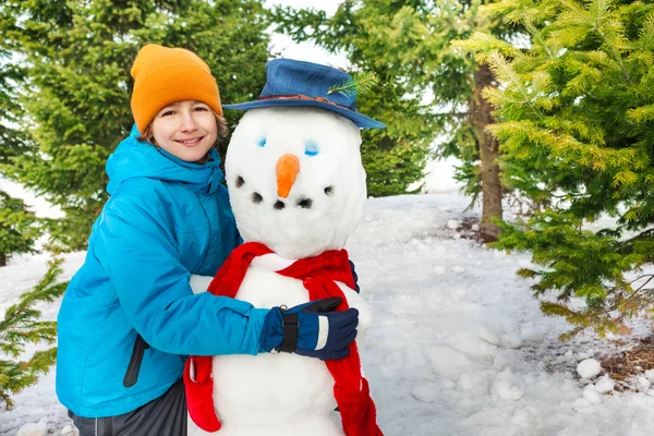 Jongen bouwt sneeuwpop met rode sjaal — Stockfoto