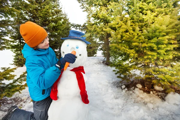 Jongen zet wortel op snowman — Stockfoto