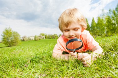 boy with magnifier laying on grass clipart