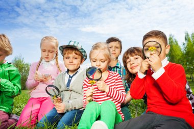 Cute children sit in meadow with magnifiers clipart