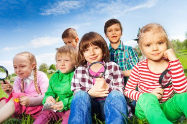 Cute children sitting on grass with magnifiers clipart