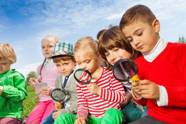 children sitting in field with magnifiers clipart