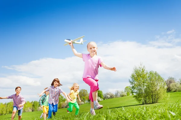 Girl holds airplane with kids running — Stock fotografie