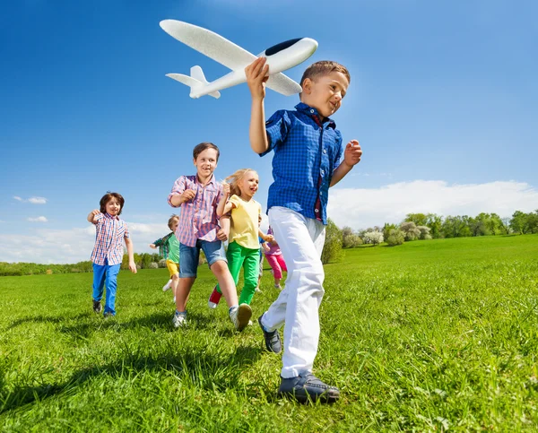 Menino segurando avião e crianças atrás — Fotografia de Stock