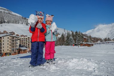 Çocuklar her biri beyaz bir kartopu tutarken ışıldıyor. Sabah güneşi yumuşak yamaçta uzun gölgeler bırakıyor.