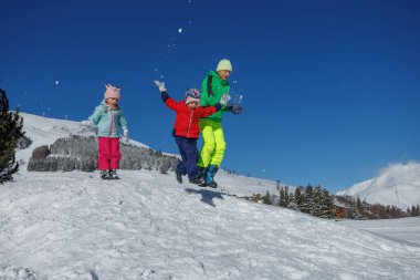 Üç genç, parlak kış giysileri içinde, tozlu karın içine atlarlar.