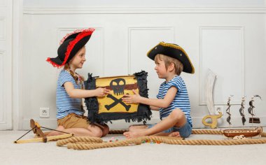 Korsan kostümleri içinde, iki genç çocuk süslü bir sandıkla oynuyorlar. Kafatası, çapraz kemikler, etrafları şeker ve oyuncak yelkenlilerle çevrili.