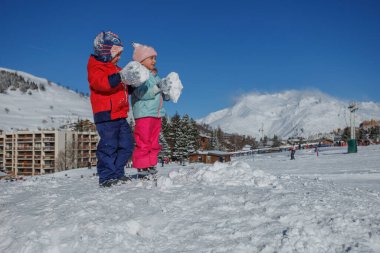 Kartoplarını doldurulmuş yamaçta yapmak için birlikte çalışırlar. Renkli ceketleri beyaz alanla canlı bir şekilde zıtlaşır.