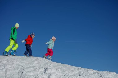Kışlık giysiler içindeki üç kardeş mavi gökyüzünün altındaki kar sırtında koşuyor. Kopya alanı olan bir görüntü.