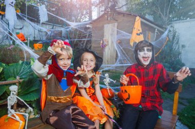 Korsan ve peri kostümlü iki çocuk iskelet boyalı arkadaşlarının yanına oturur ve turuncu kovada şeker ararlar.