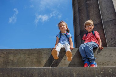 Mavi gökyüzünün arka planında, İskoçya Ulusal Anıtı 'nın taş basamaklarında iki çocuk mutlu bir şekilde oturuyor.
