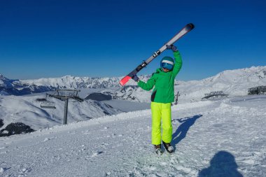 Bir kayakçı kayakları karların üstünde bir açıyla kaldırır. Uçsuz bucaksız dağların zirveleri açık gökyüzünün altında uzanır.