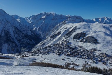 Karla kaplı bir köy. Mavi gökyüzünün altında görkemli dağların arasına kurulmuş bir kayak merkezi.