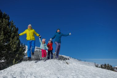 Açık gökyüzünün altında, bir aile neşeli bir şekilde karda koşuyor, parlak ve renkli kış kıyafetleri içinde, Noel tatillerinde eğleniyorlar.