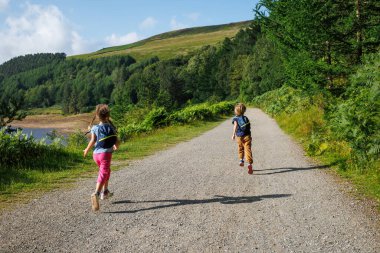 Güneşli bir ormanın ortasında, iki çocuk doğa yürüyüşçüsü, sırt çantaları ile İngiltere 'nin Yukarı Derwent Vadisi' ndeki çakıl taşlı patika boyunca yarışıyor.