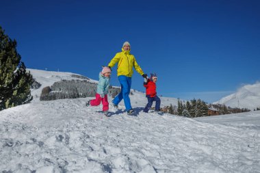 Neon yeşili giyen bir ebeveyn, kar tarlasında kırmızı ceketli iki çocuğa liderlik ediyor..