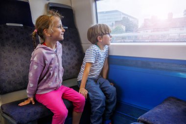 Trenin içinde, genç bir kız ve oğlan yolculuklarının tadını çıkarırken o parlak pembe bir pantolon giyer, o ise çizgili bir spor gözlüğü takar.