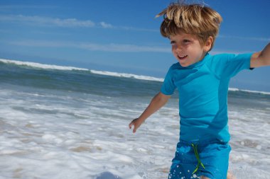 Deniz köpüğü sahile yaklaşırken, küçük çocuk yaz tatillerinde sevinçle sahili boydan boya geçer.