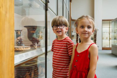 Kültür okulu gezisinde cam arkasında sergilenen tarihi eserlere bakan iki çocuk.