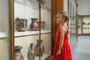 Bir müze ortamında, iki genç cam arkasında sergilenen ve süslemeleriyle ilgilenen devasa tarihi gemileri inceliyor.