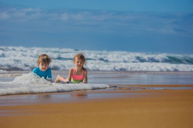 İki çocuk yaz tatilinde, güneşli bir sahilde dalgalarla oynamaktan keyif alır. Dalgalar içeri girerken gülüp eğlenirler. Çevrelerini keşfederken kumsalda köpük oluştururlar.