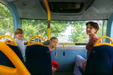 Bir erkek ve bir kız otobüste bir yetişkinle oturuyorlar, şehirde mutlu bir şekilde seyahat ediyorlar.